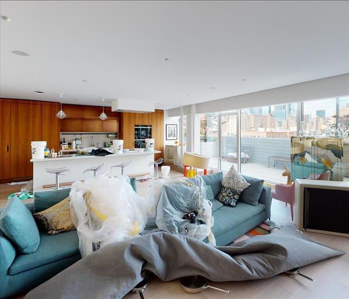 Sealed and covered kitchen contents on living room table. The kitchen behind the living area appears water-damaged, with seve