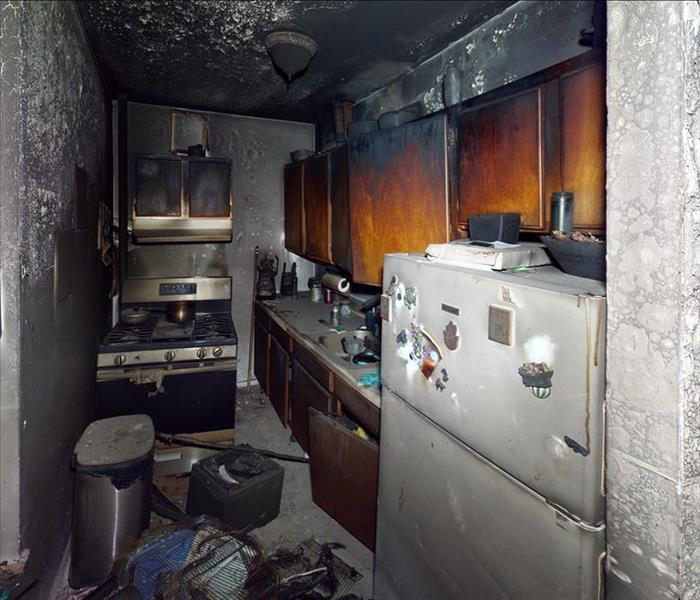 A heavily fire-damaged apartment kitchen with charred walls, fixtures, and contents