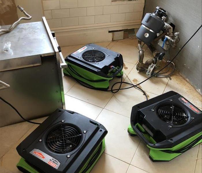 kitchen base cabinets removed, showing the garbage disposal on the floor with several pieces of drying equipment